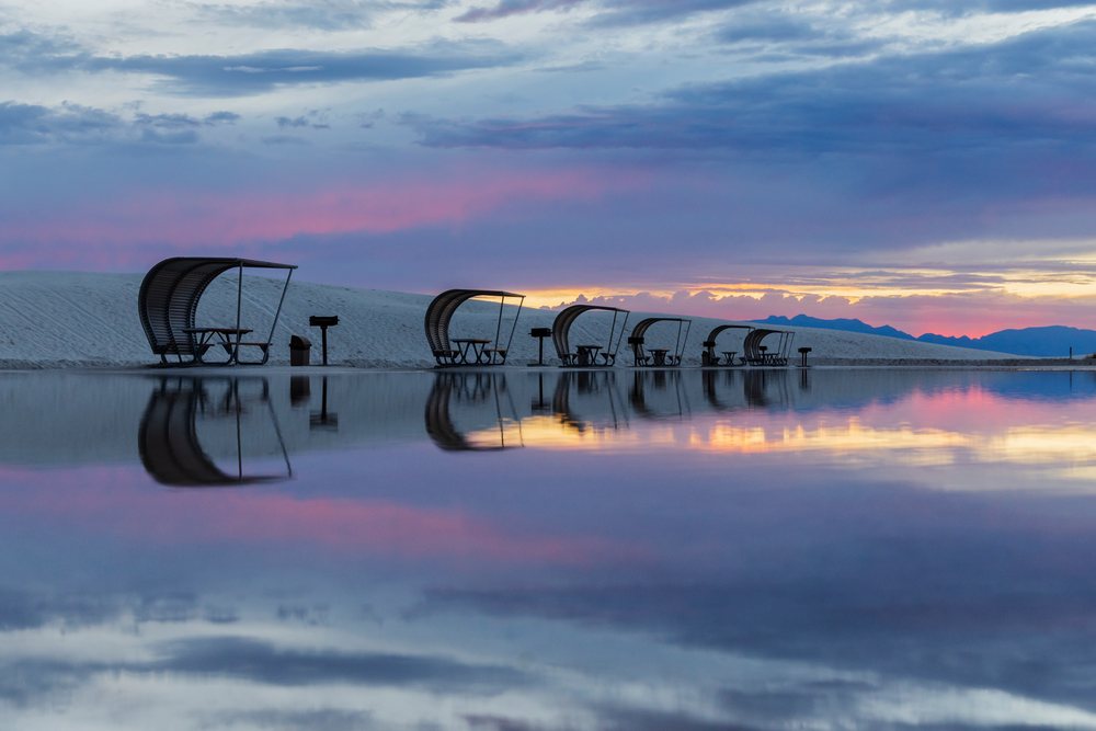 Picnic shelters with curved roofs reflected in water at sunset, with sand dunes and mountains at white Sands National Monument, Landscape, Wildlife, Alamogordo, New Mexico, USA.