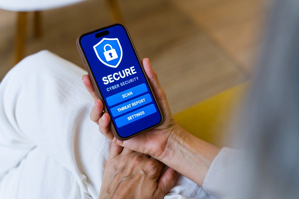 Hand holding smartphone displaying a secure cyber security app with scan, threat report, and settings options indoors, Spain.