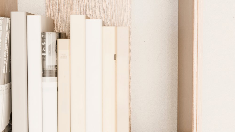 Books with neutral-toned spines arranged vertically on a wooden bookshelf indoors.