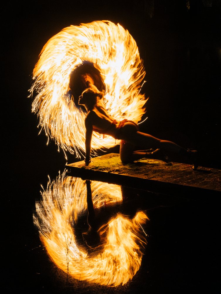 Fire performer spinning flaming hoop creates vivid reflection on water at night, artistry, artist, USA.