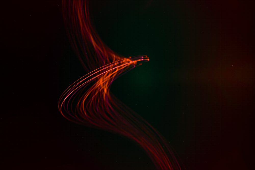 Curved red light trails captured with long exposure creating abstract glowing patterns on a dark background.