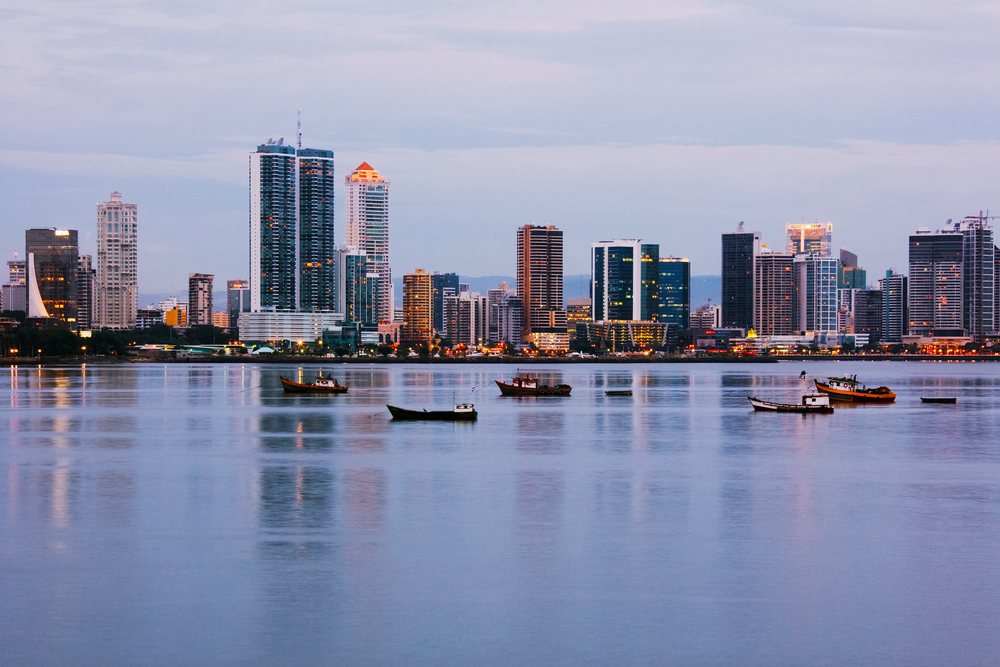 Panama City skyline at dusk with boats on calm harbor water reflecting city lights, Casco Viejo.