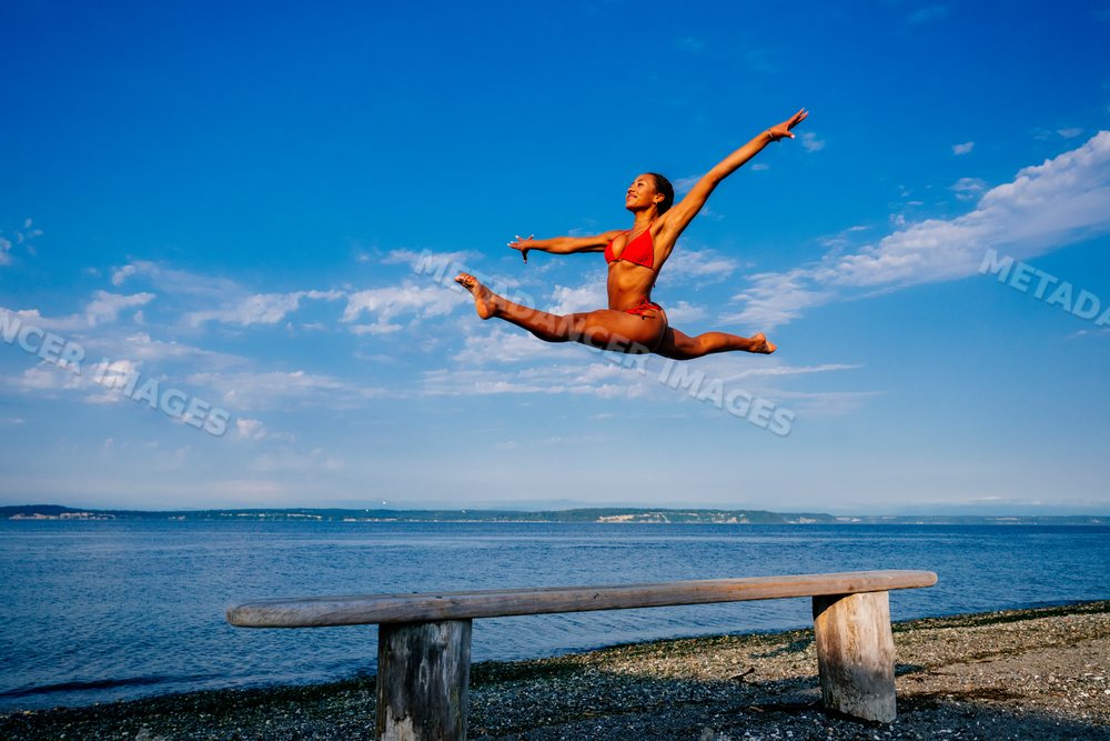 A woman leaps in a split over a beam on a beach in WA, USA