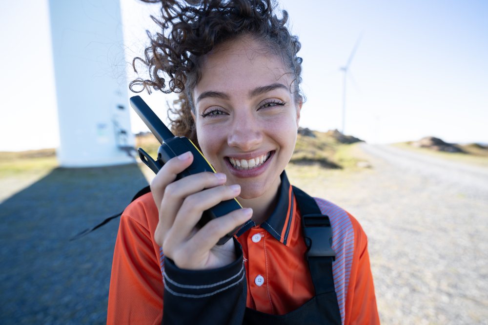Woman smiling and holding a walkie talkie outdoors near wind turbines at a wind farm, sustainability, renewable energy, Galicia, Spain.