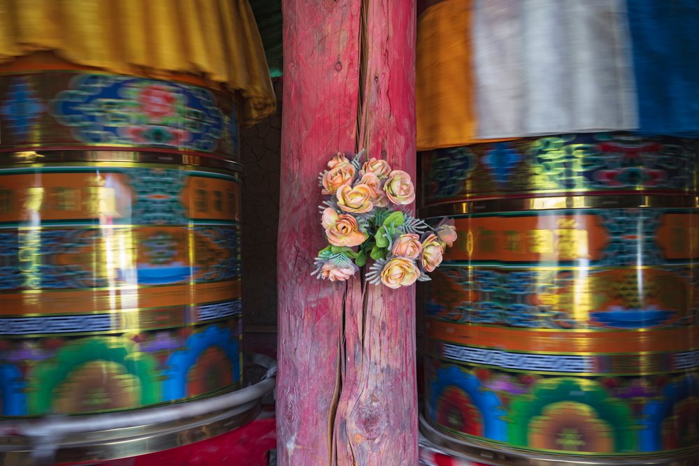Two large spinning Tibetan Prayer Wheels decorated with peach artificial flowers on a wooden post in Kham Tibet, China, Dongpojia, Sichuan Province, People's Republic of China.