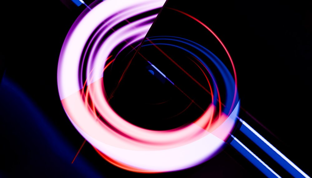 Colorful glowing light trails forming circular patterns on a dark background creating an abstract artistic effect.