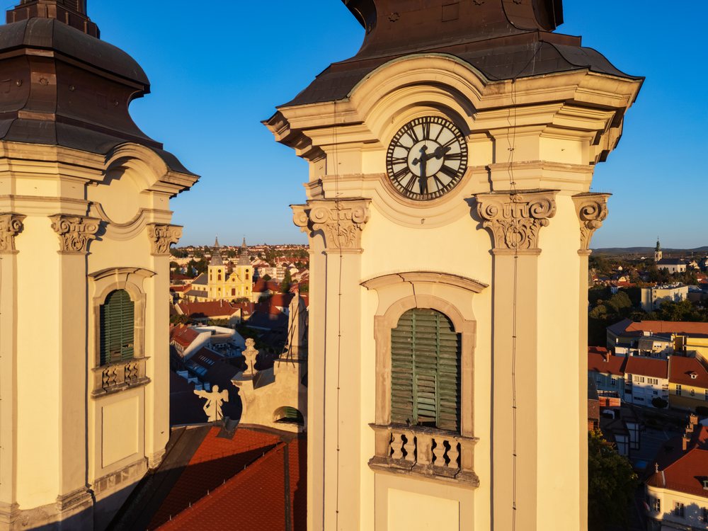 Sunrise illuminates the Baroque towers of the Minorite Church, with clear sky and cityscape in the background, Eger, Hungary.