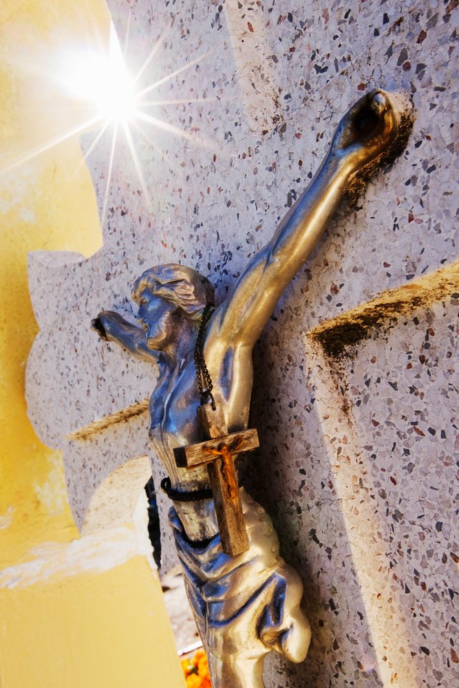 Metal crucifix of Jesus mounted on a textured stone headstone.