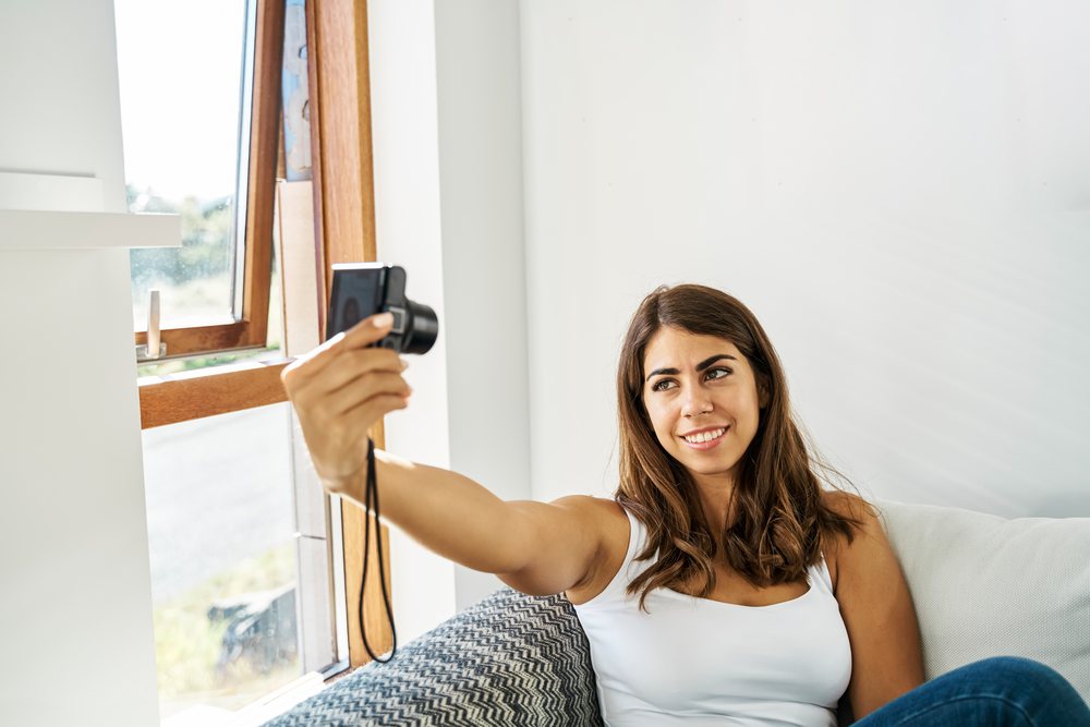 Young white woman sitting on a couch taking a selfie with a digital