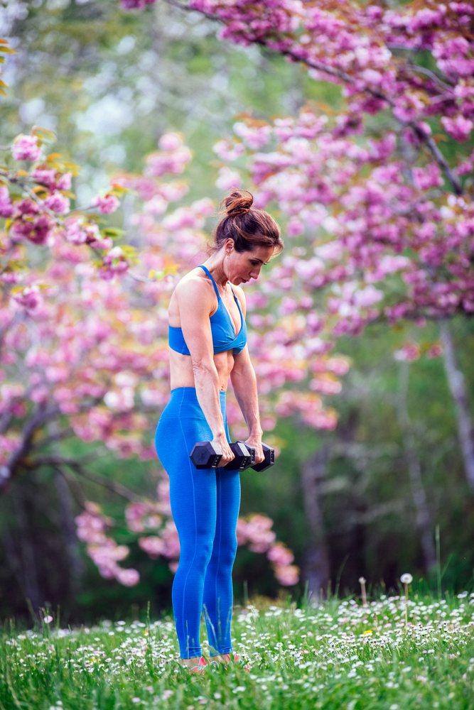 Woman performing calisthenics with dumbbells outdoors among blossoming trees in spring, USA.