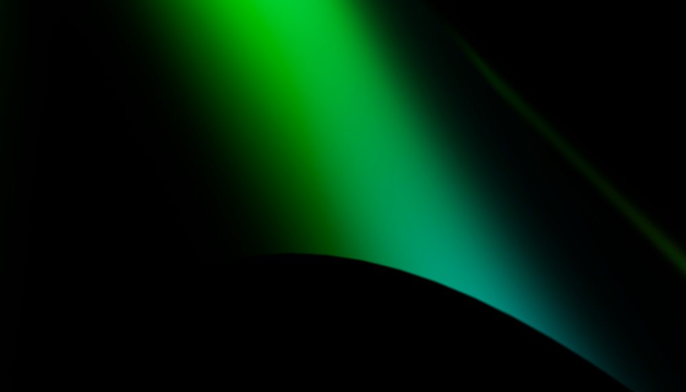 Green light creates a glowing gradient over a dark curved surface with soft ambient illumination.