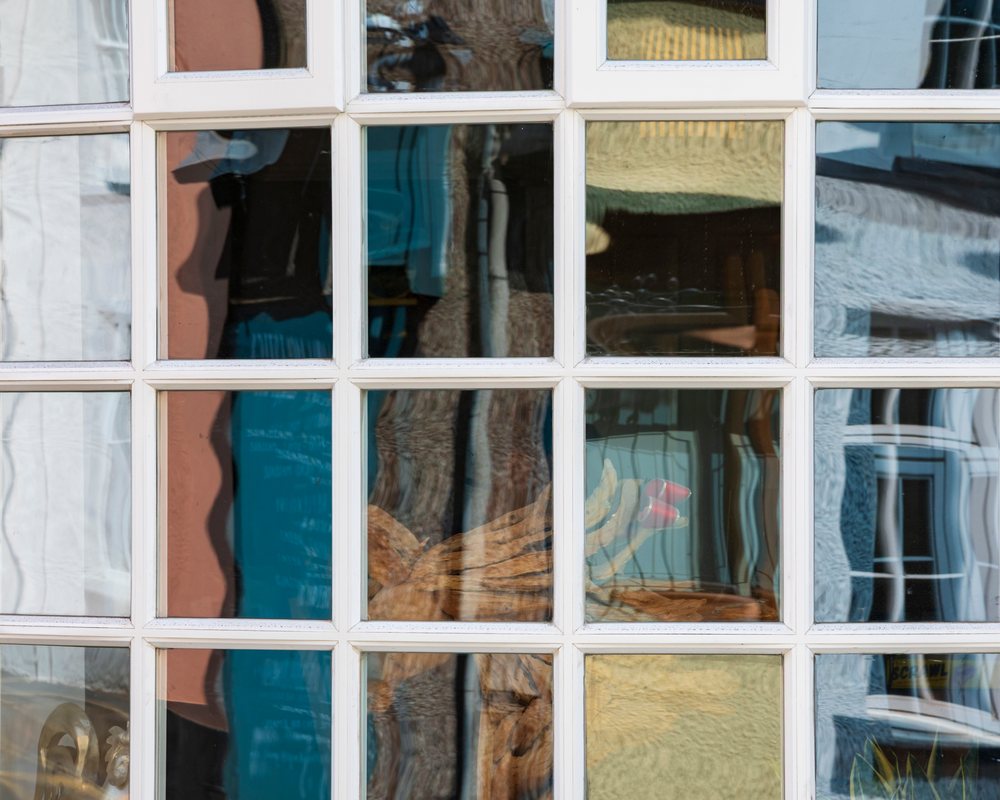 House window with multiple square panes showing distorted reflections of blue and yellow walls, buildings, and a wooden sculpture, Landscape, Crickhowell, Powys, Wales.