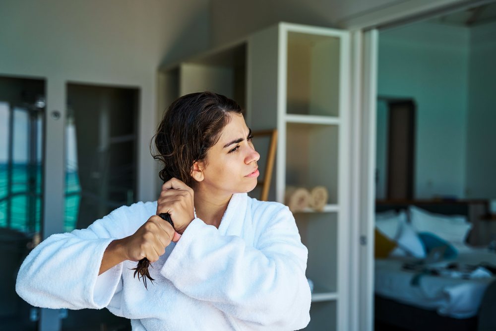 A woman in a white bathrobe combs her wet hair in a hotel room in the, Maldives.