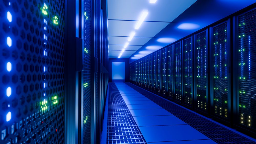 Corridor in a server room with rows of glowing server racks under blue lighting and visible grated floor vents.