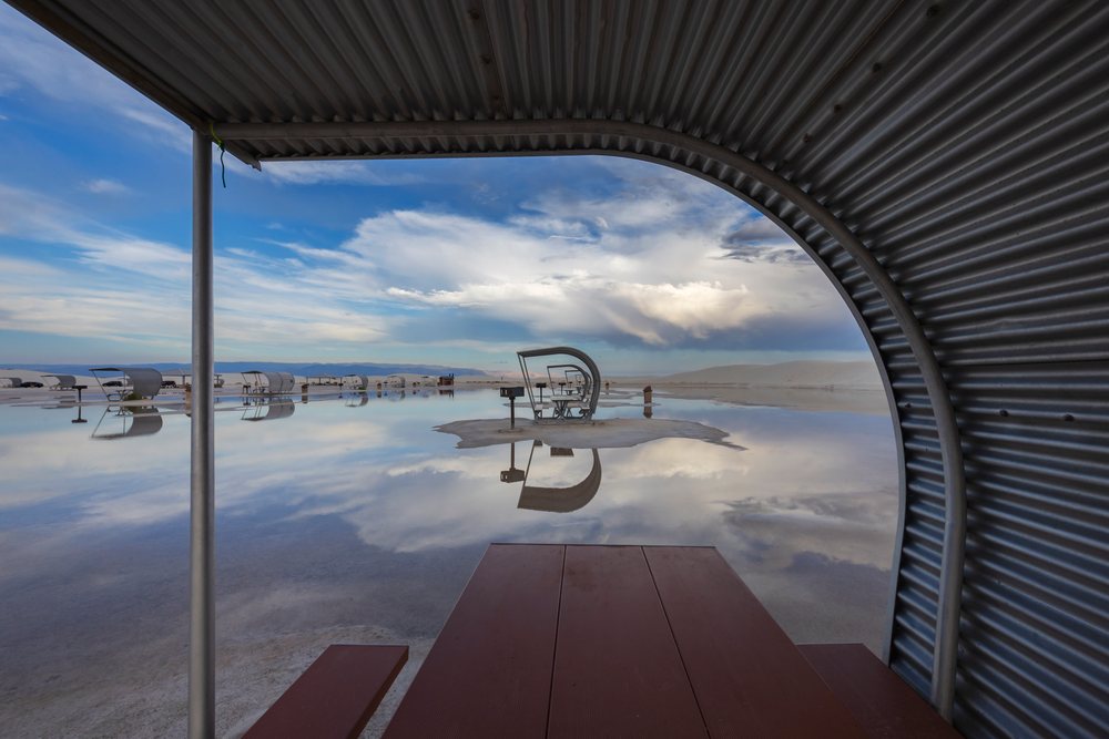Metal picnic shelters with brown tables and benches reflected on wet sand at white Sands National Monument, Landscape, Wildlife, Alamogordo, New Mexico, USA.