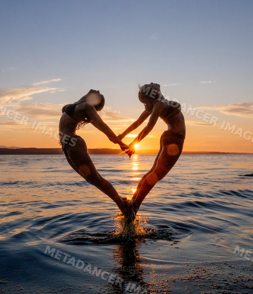 Two women performing partner acrobatics yoga at sunset over water