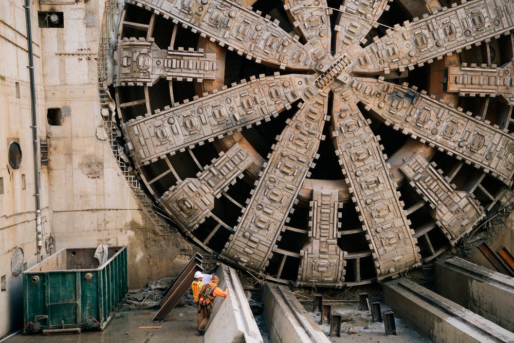 Two construction workers inspect a large tunnel boring machine during an underground drilling project, USA.