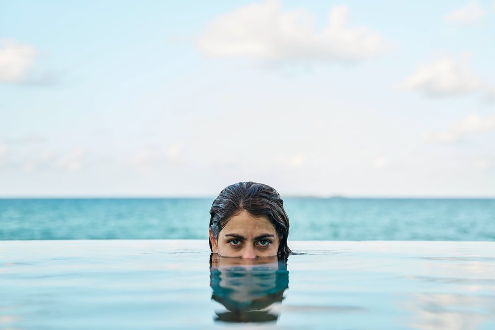 A white woman swimming in an infinity pool overlooking the ocean