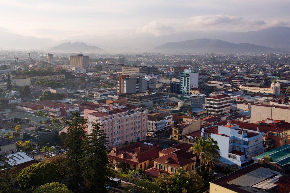 Cityscape showing urban buildings, streets, and mountains under a hazy sky on a morning, San Jose, Costa Rica.