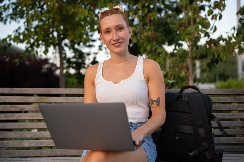 A woman with an animal tattoo on her arm uses a laptop while sitting on a bench outdoors, urban, Santiago De Compostela, Spain.