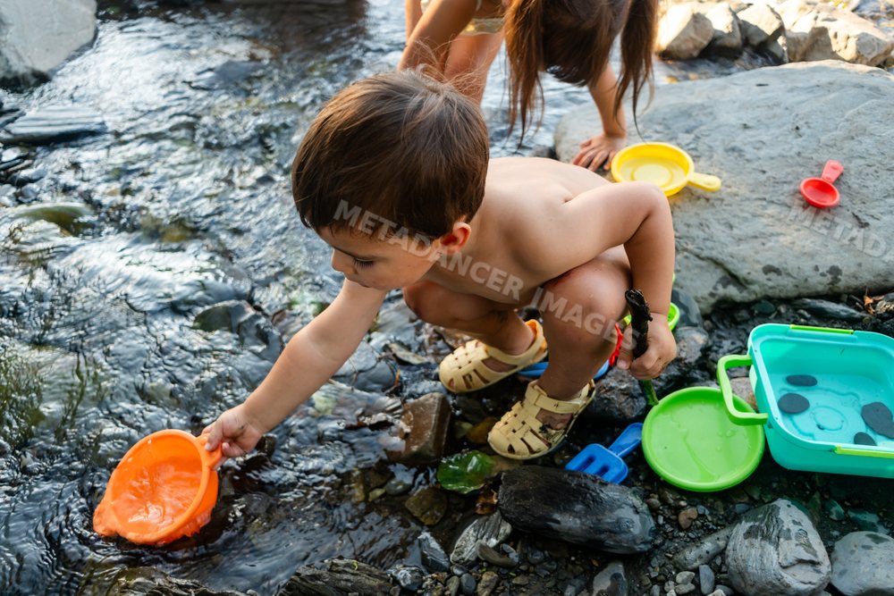 Young white boy playing with water toys on a rocky riverbank