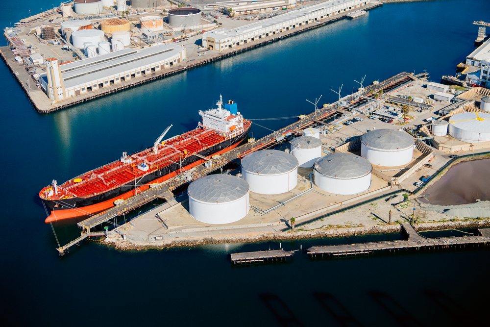 Oil tanker docked alongside industrial storage tanks and facilities at the Port of Long Beach, California, CA, USA.