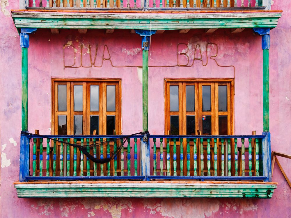 Colorful pink building facade with wooden shutters and green and blue balcony railings, Cartagena, Columbia.