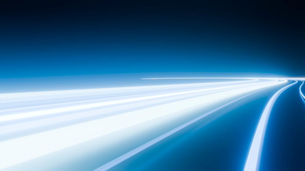 Blue-toned light trails curve along a highway at night, illustrating motion and speed with dynamic blur effects.