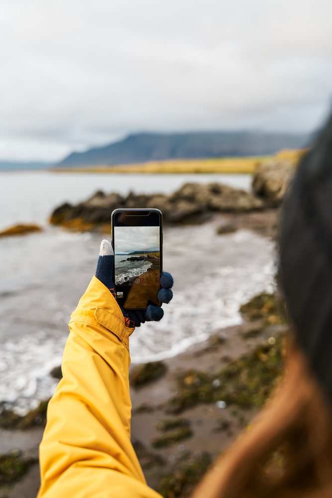 White Person taking photo of rocky coastline and sea on Iceland shore
