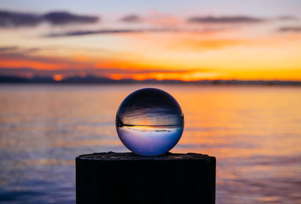 Crystal ball on a wooden post reflects a colorful sunset over calm water, Norwegian Point, WA, USA.