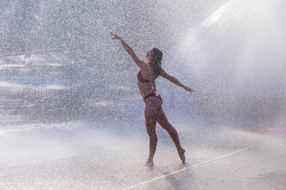 Woman in a bikini dancing and posing in water spray outdoors, partner, acrobatics, yoga, USA.