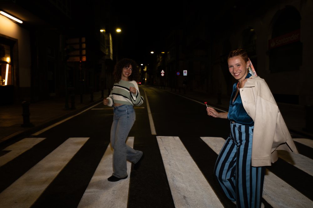 Two women share laughter and friendship while walking across a city crosswalk at night, Santiago De Compostela, Spain.