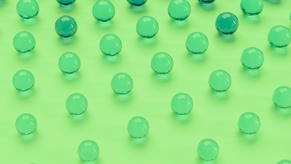Green transparent spheres arranged on a green surface forming an abstract geometric pattern with shadows and reflections.