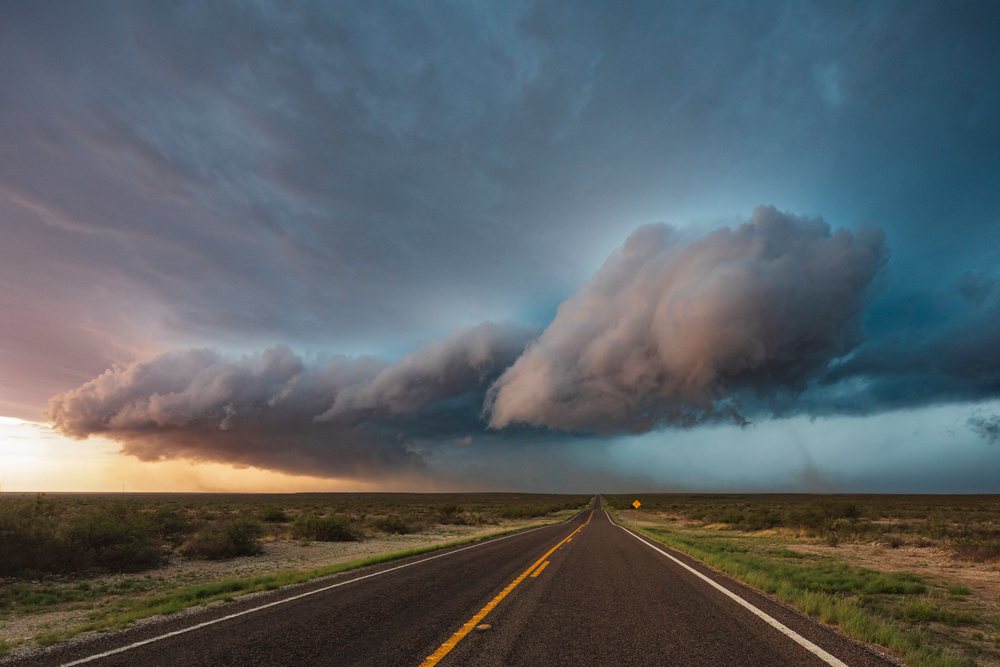 Supercell storm cloud forms over an open asphalt road, within the Great Plains region of the USA at sunset, Sanderson, Texas.