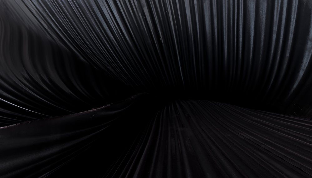 Black fabric with deep folds and smooth texture creates abstract dark shadows.