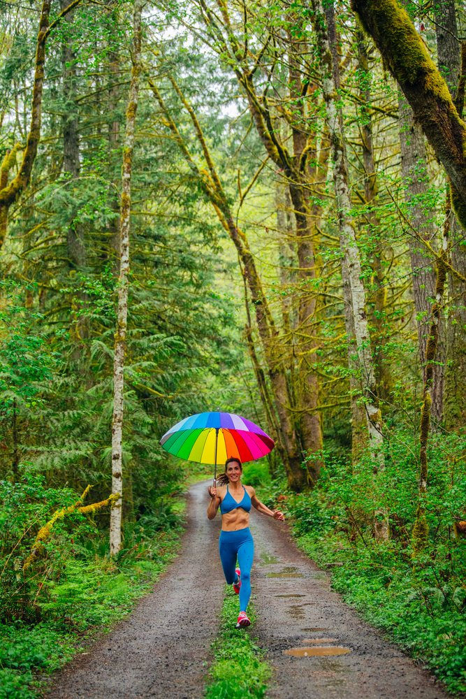 Woman running on a forest trail in the USA holding a rainbow umbrella during outdoor exercise, Calisthenics.