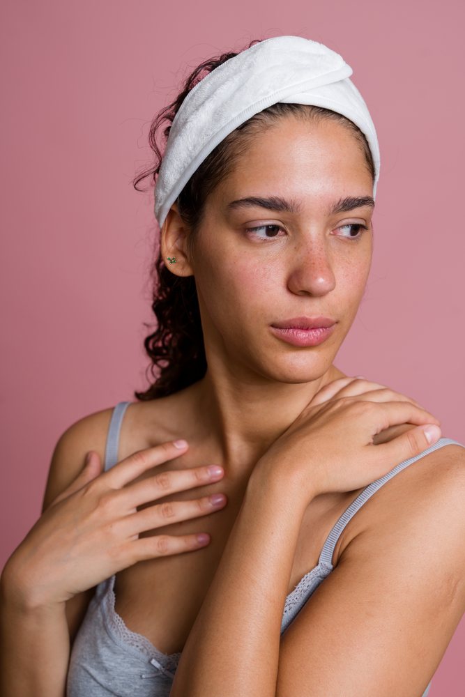 Woman with freckles and a white cotton headband poses against a pink background in a beauty shoot, Spain.