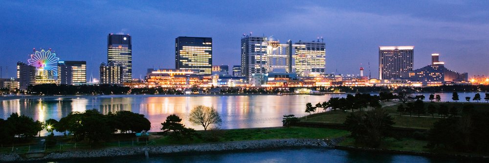 Aqua City and Fuji TV Building illuminated at night reflecting on water in Odaiba, Tokyo, Japan.