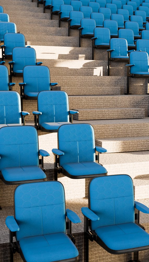 Blue theater seats with armrests arranged on stepped flooring in an indoor auditorium or event space.