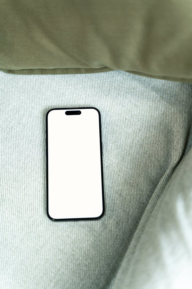 Top view of a smartphone with blank white screen on green textured fabric surface indoors, mock up, Spain.