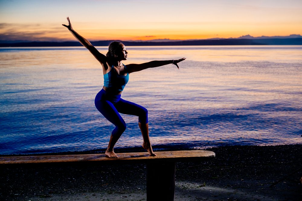 Woman practicing a yoga balance pose on a bench at sunset on a beach, USA.