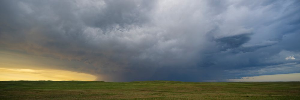 Receding Storm clouds move away over an open grassy prairie landscape with wide horizon, Sutherland, Nebraska, USA.
