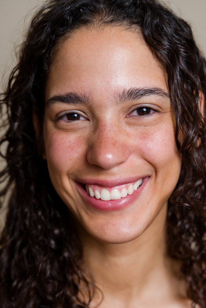 Close-up portrait of a smiling woman with curly hair and freckles, beauty shoot, Spain.