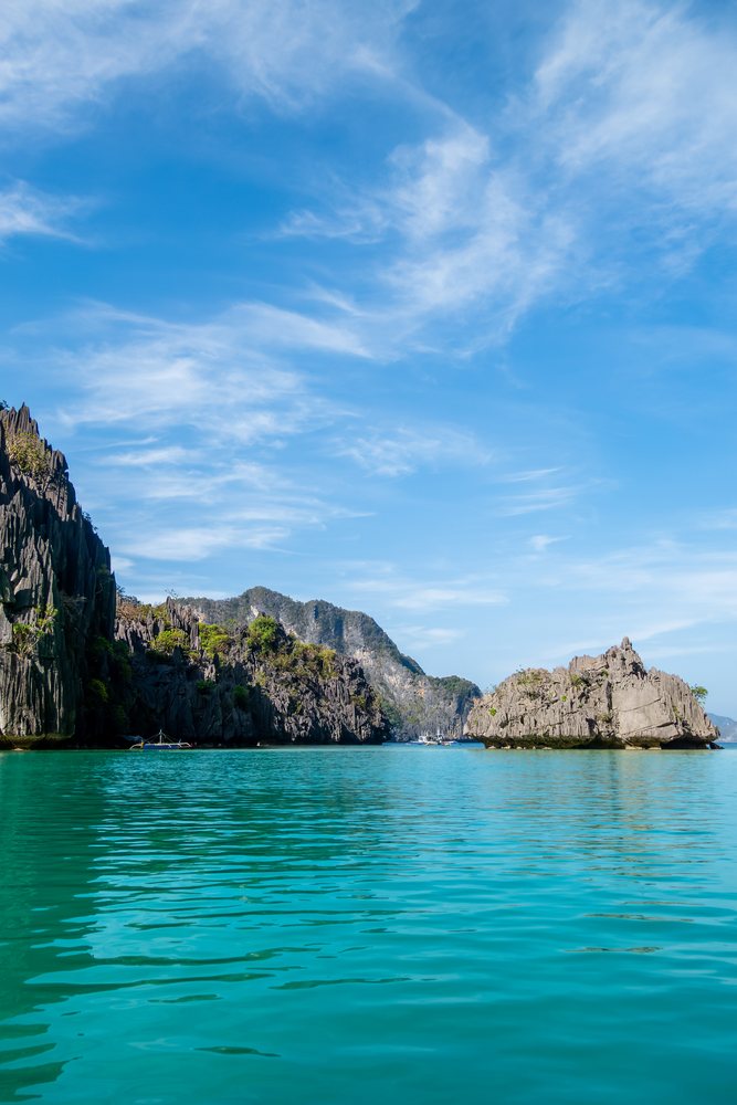 Turquoise ocean water and limestone cliffs form a scenic tropical seascape under a bright blue sky, Philippines.