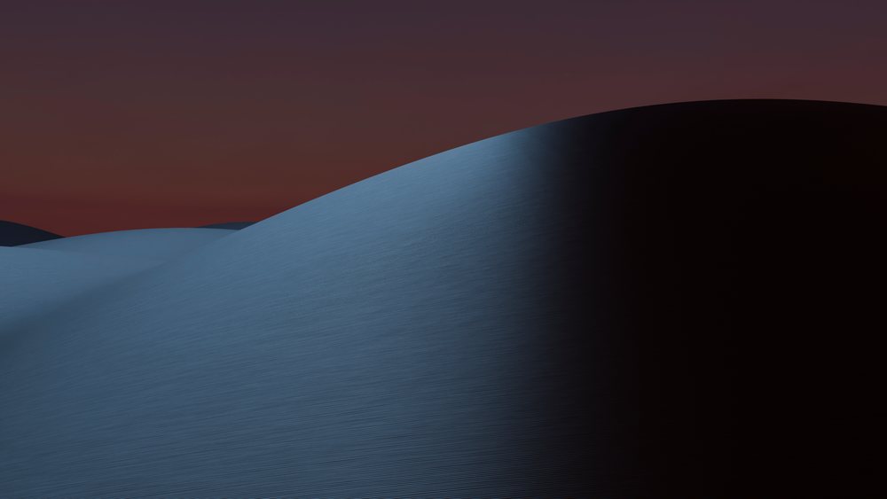 Sand dunes casting shadows under a deep evening sky at sunset in a desert landscape.