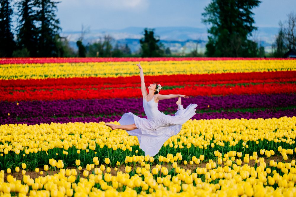 Ballet dancer in a white dress leaps gracefully in a colorful tulip field outdoors in the USA during spring.