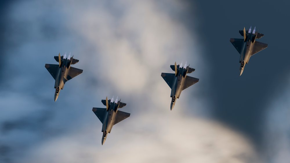 Four fighter jets fly in close formation with afterburners visible against a cloudy sky, defense, war, security, military.