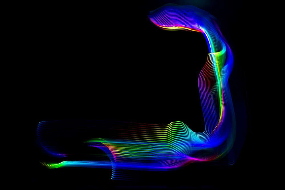 Multicolored curved light streaks form a rainbow spectrum against a dark background using light painting.