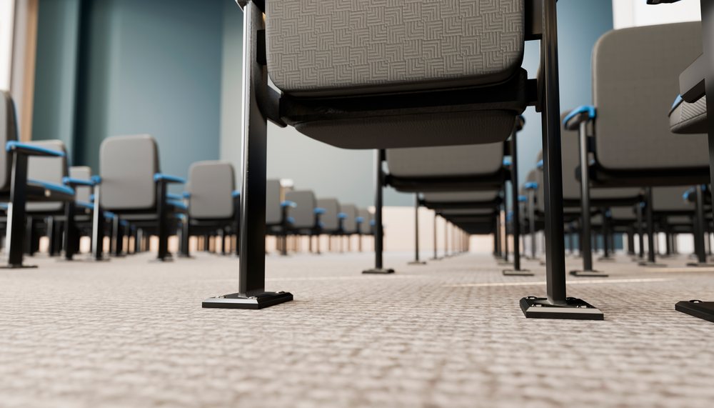 Multiple gray conference chairs with blue armrests arranged in rows on a textured carpeted floor in an indoor meeting room.