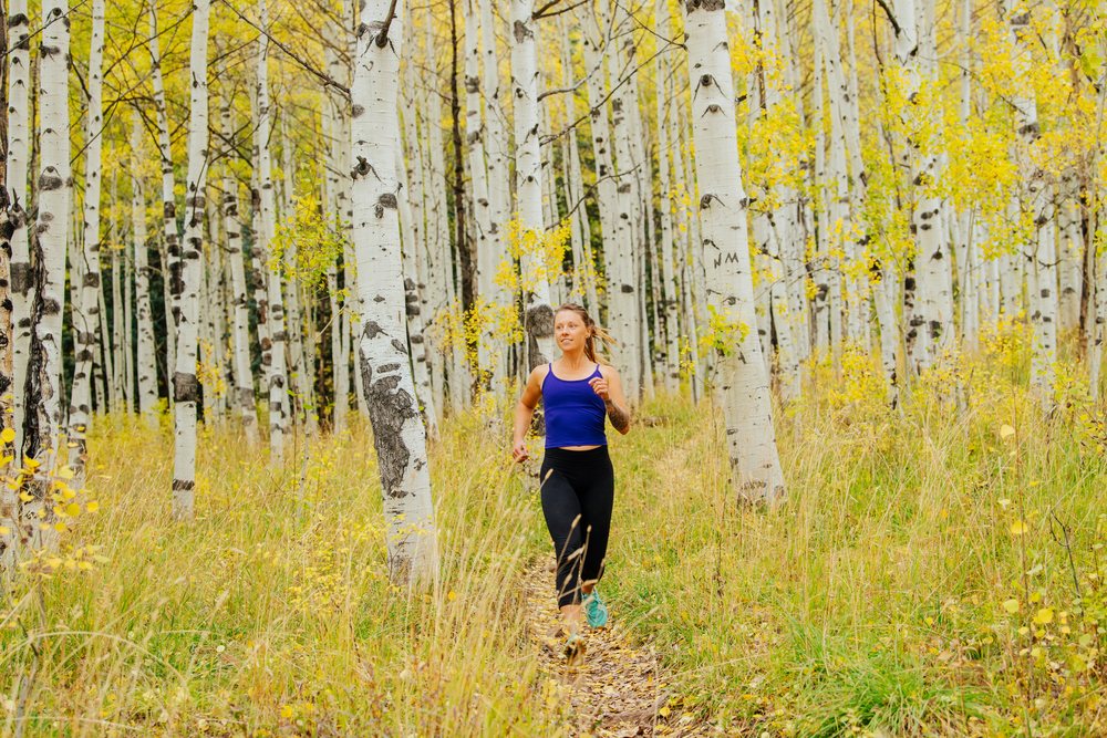 Woman running on a trail through birch trees with yellow autumn leaves, fall colors, Durango, Colorado, USA.